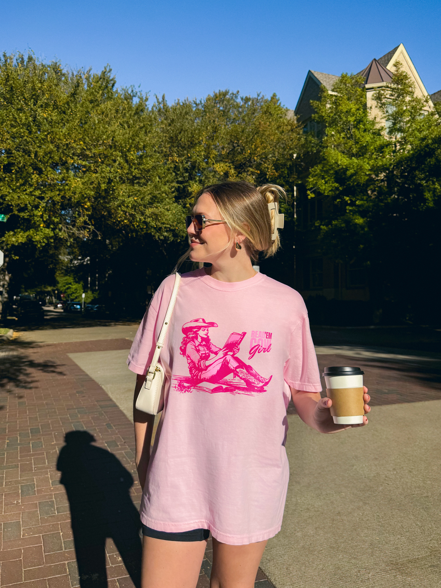 Woman wearing an ivory Comfort Colors graphic t-shirt featuring a pink cowgirl reading a book with “Read ’Em Cowgirl” text