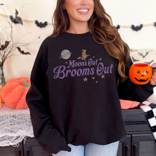 Crewneck sweatshirt with a simple witch and full moon graphic and retro inspired font that reads Moons out Brooms out in purple.