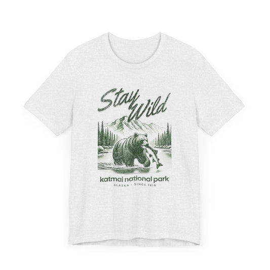 A graphic t-shirt featuring an Illustration of a grizzly bear fishing in Katmai National Park with "Stay Wild" text – Alaska Since 1918