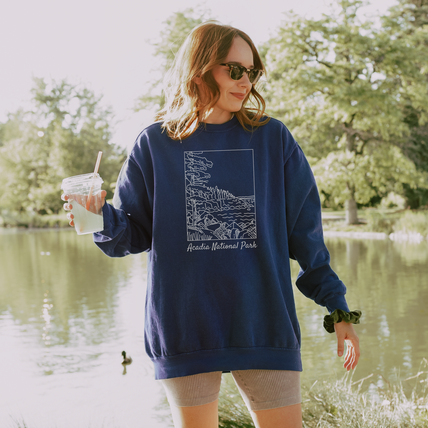 Comfort Colors 1566 Crewneck Sweatshirt with a white illustration graphic of a scene from Acadia National Park. The graphic reads "Acadia National Park" under the image.