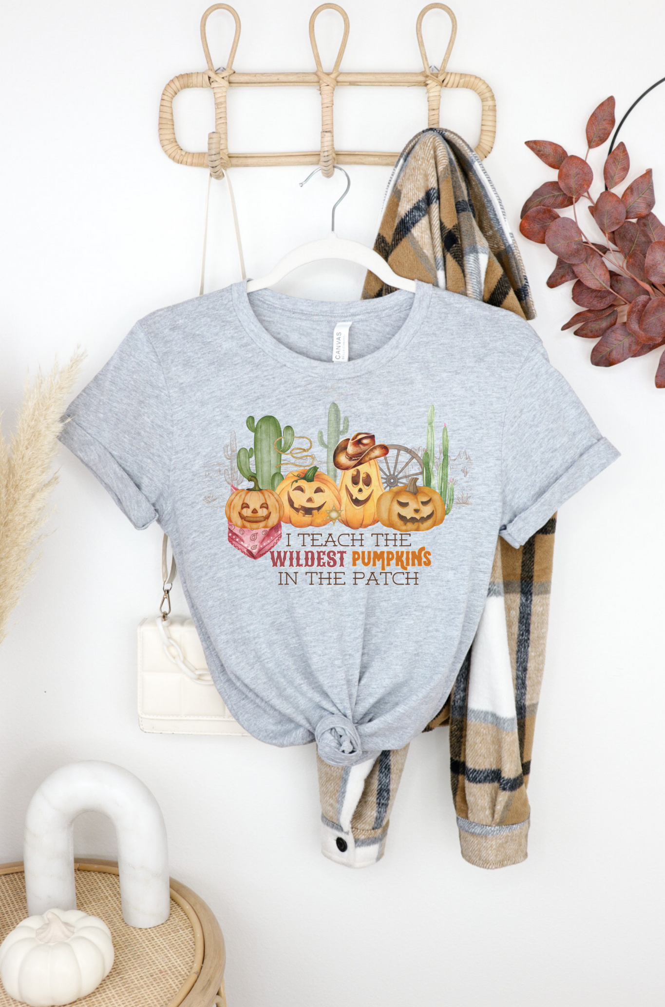 Bella Canvas 3001 Tshirt with a western halloween scene of jack o lanterns wearing western gear in the desert. The graphic reads I teach the wildest pumpkins.