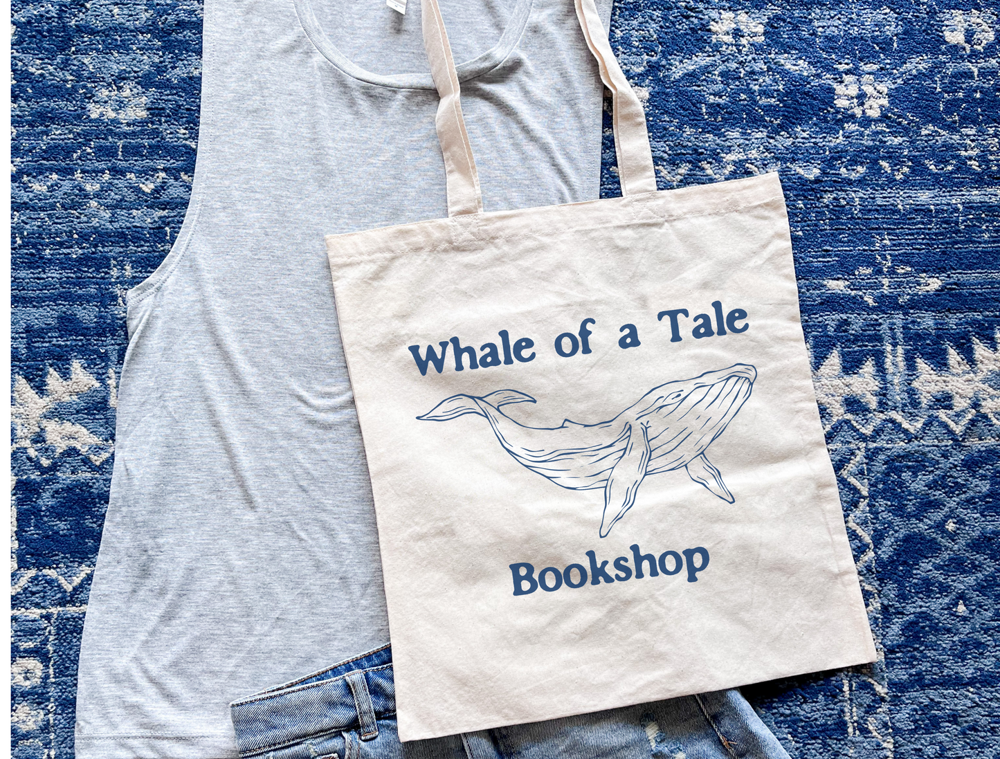 A canvas tote bag with a navy blue DTG graphic that features a whale and reads "Whale of a Tale Bookshop"