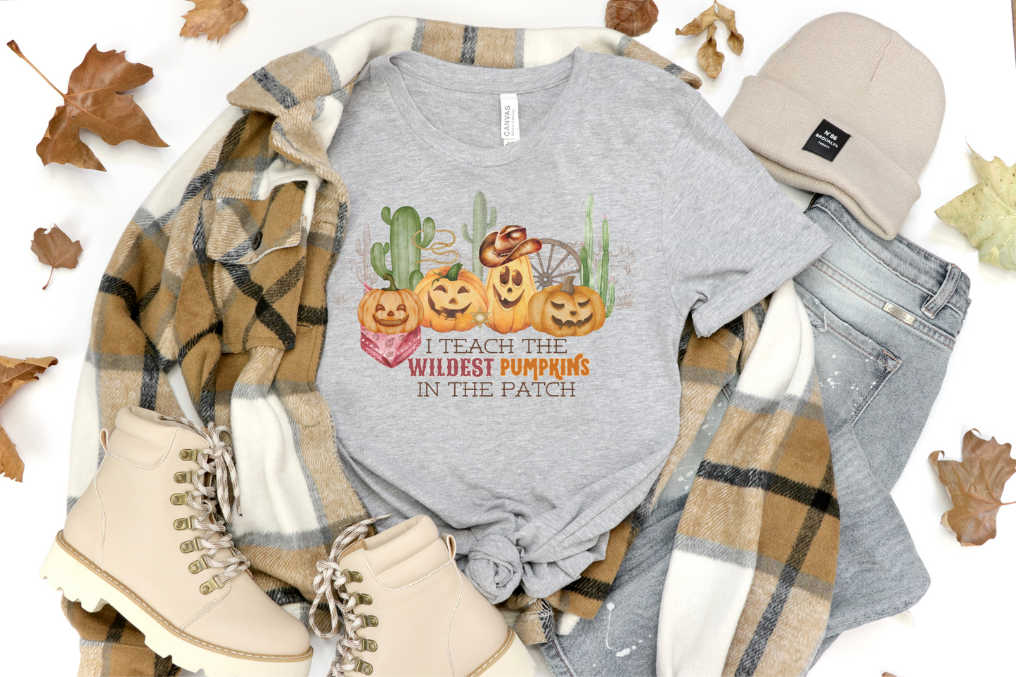 Bella Canvas 3001 Tshirt with a western halloween scene of jack o lanterns wearing western gear in the desert. The graphic reads I teach the wildest pumpkins.