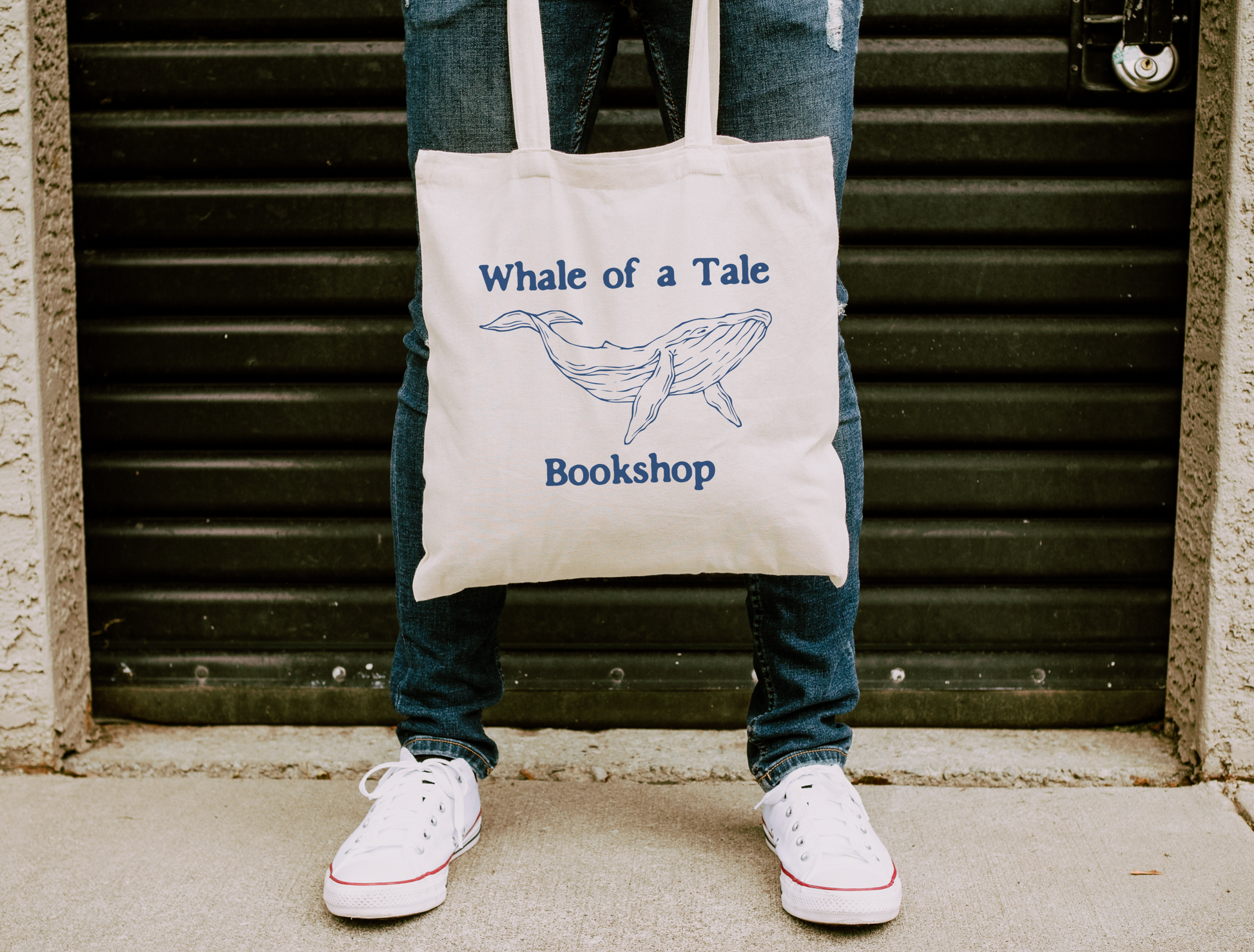 A canvas tote bag with a navy blue DTG graphic that features a whale and reads "Whale of a Tale Bookshop"