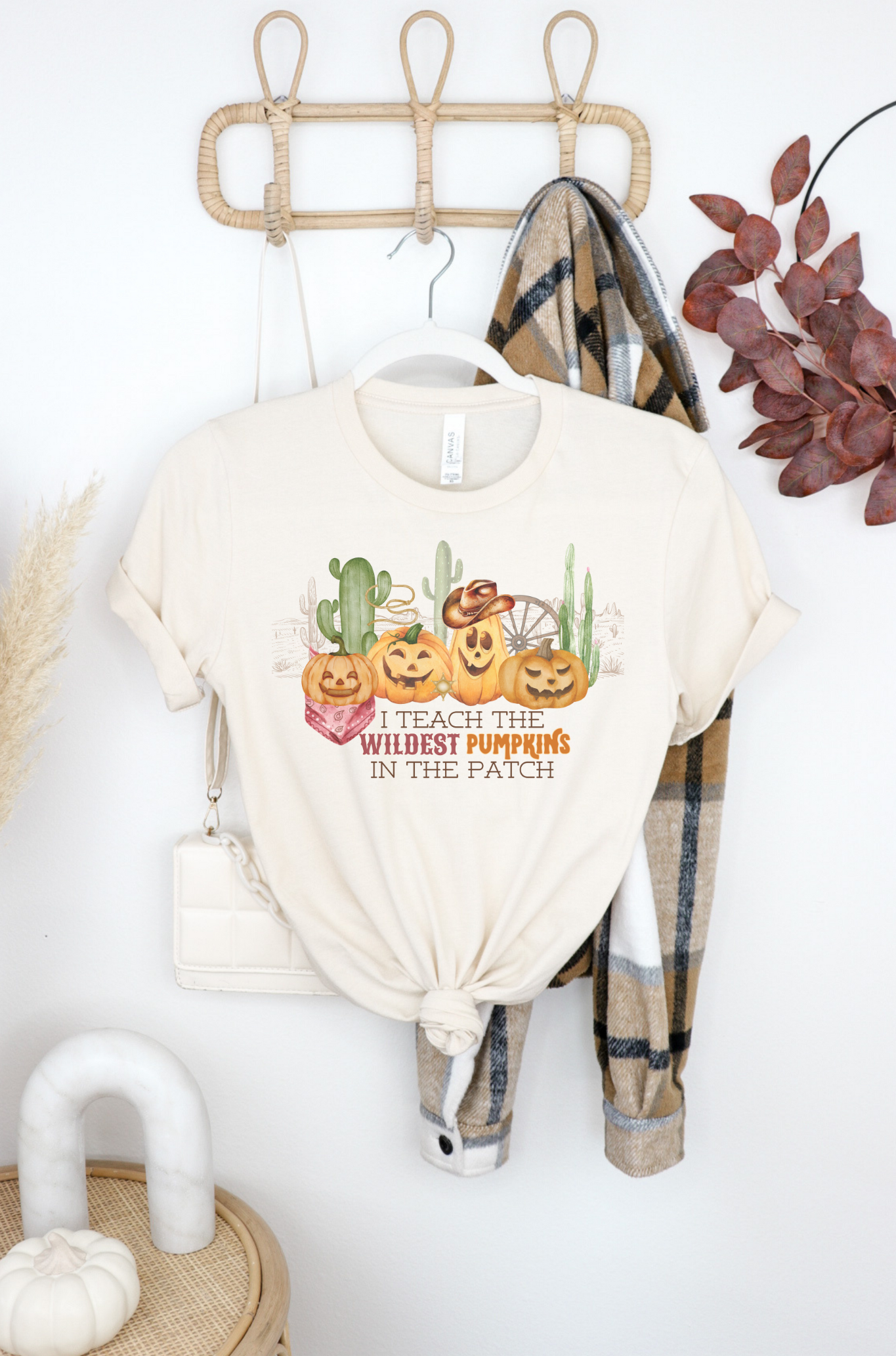 Bella Canvas 3001 Tshirt with a western halloween scene of jack o lanterns wearing western gear in the desert. The graphic reads I teach the wildest pumpkins.