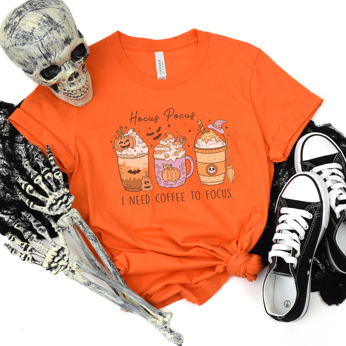 A Bella+Canvas 3001 Tshirt with a Halloween graphic featuring 3 spooky themed coffee drinks. The graphic reads "Hocus pocus I need coffee to focus"