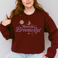 Crewneck sweatshirt with a simple witch and full moon graphic and retro inspired font that reads Moons out Brooms out in purple.