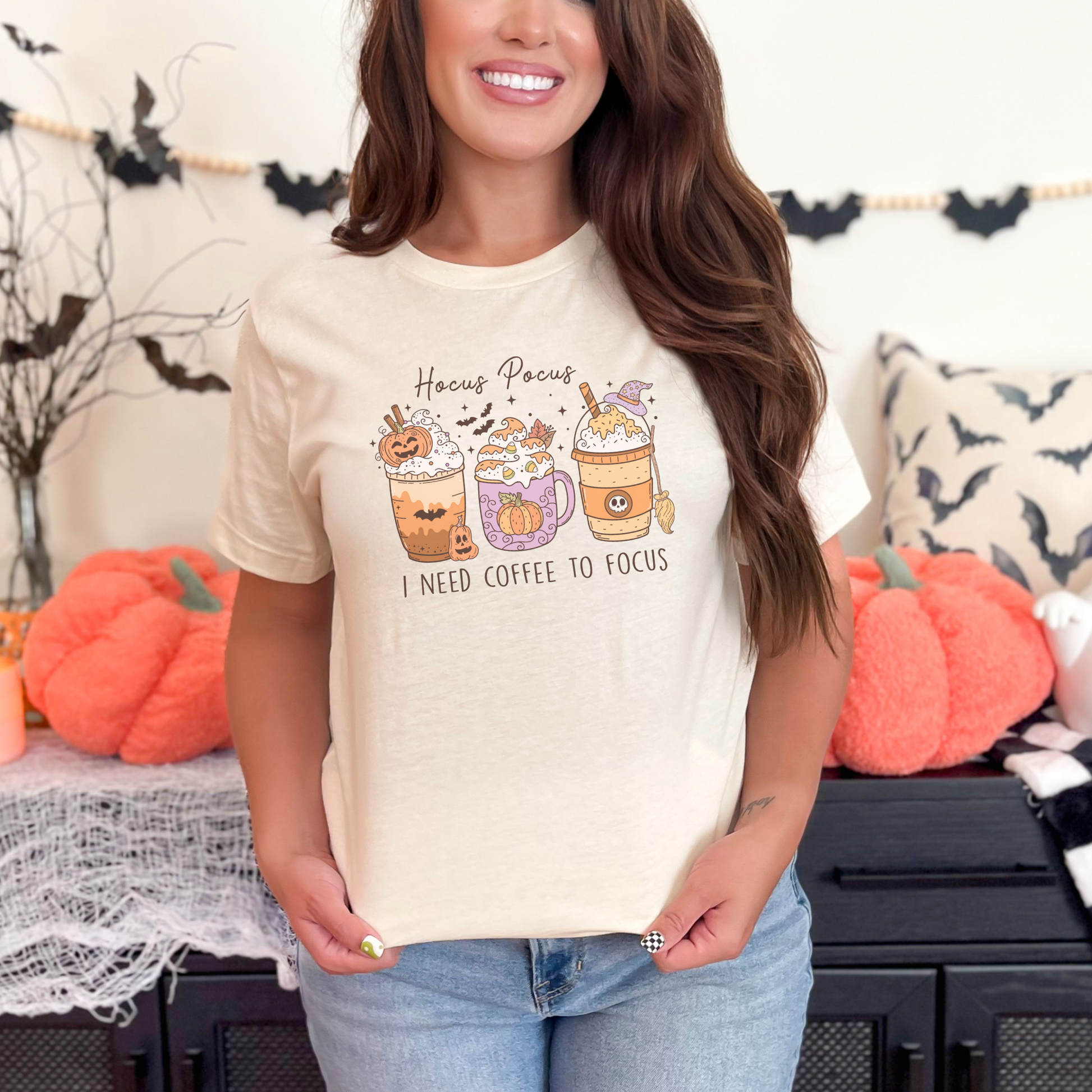 A Bella+Canvas 3001 Tshirt with a Halloween graphic featuring 3 spooky themed coffee drinks. The graphic reads "Hocus pocus I need coffee to focus"