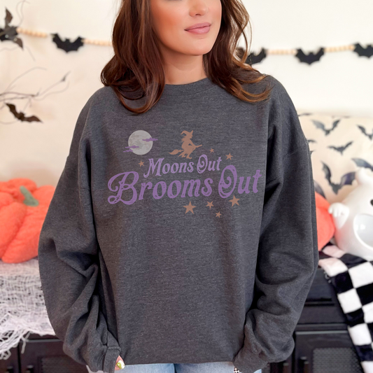 Crewneck sweatshirt with a simple witch and full moon graphic and retro inspired font that reads Moons out Brooms out in purple.