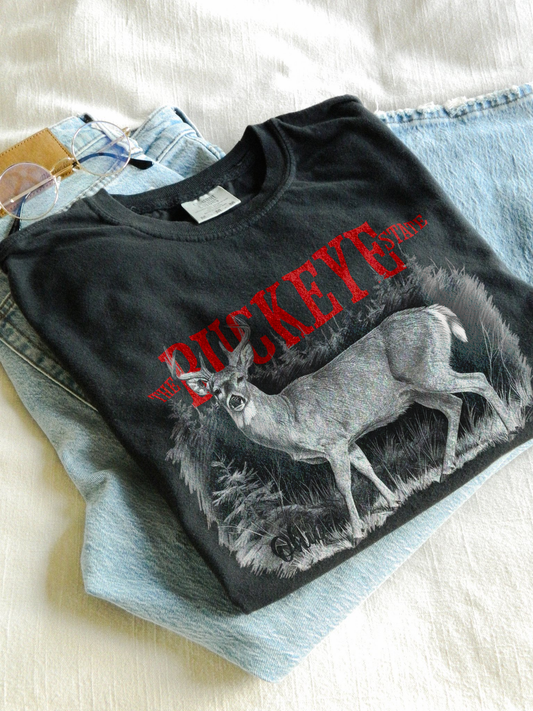 Graphic t-shirt featuring a detailed white-tailed deer illustration with bold “Buckeye State” and “Ohio” text, printed on a Comfort Colors tee.