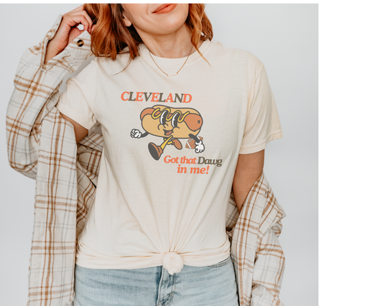 Comfort Colors Ivory Tee with Retro Hot Dog Character holding a football. The Graphic tee reads "Cleveland" Got that Dawg in Me! in Orange and Brown Text