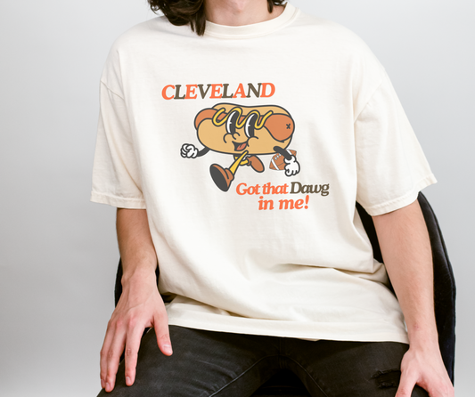 Comfort Colors White Tee with Retro Hot Dog Character holding a football. The Graphic tee reads "Cleveland" Got that Dawg in Me! in Orange and Brown Text
