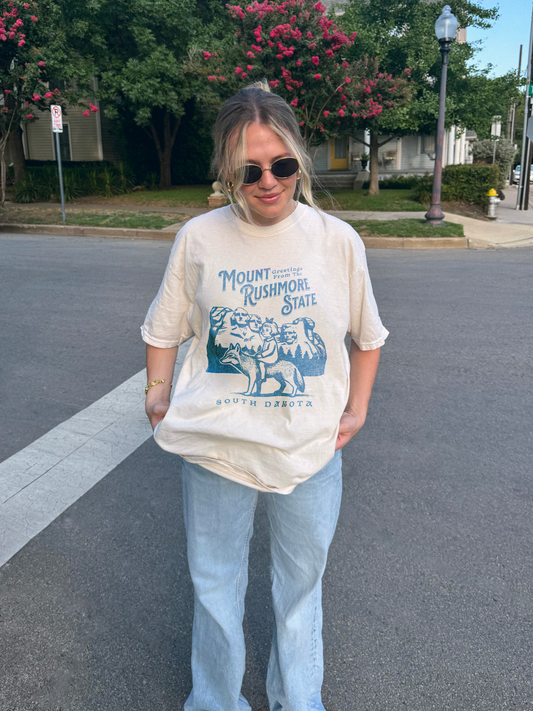 Model wearing an ivory comfort colors tshirt featuring a graphic of a girl on a fox wolf in front of mount rushmore. the shirt reads Mount Rushmore State south Dakota