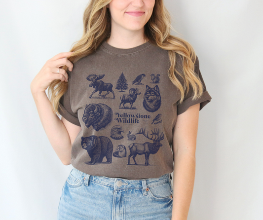 Woman wearing a soft garment-dyed t-shirt featuring vintage illustrations of Yellowstone wildlife including a bear, elk, wolf, and eagle.
